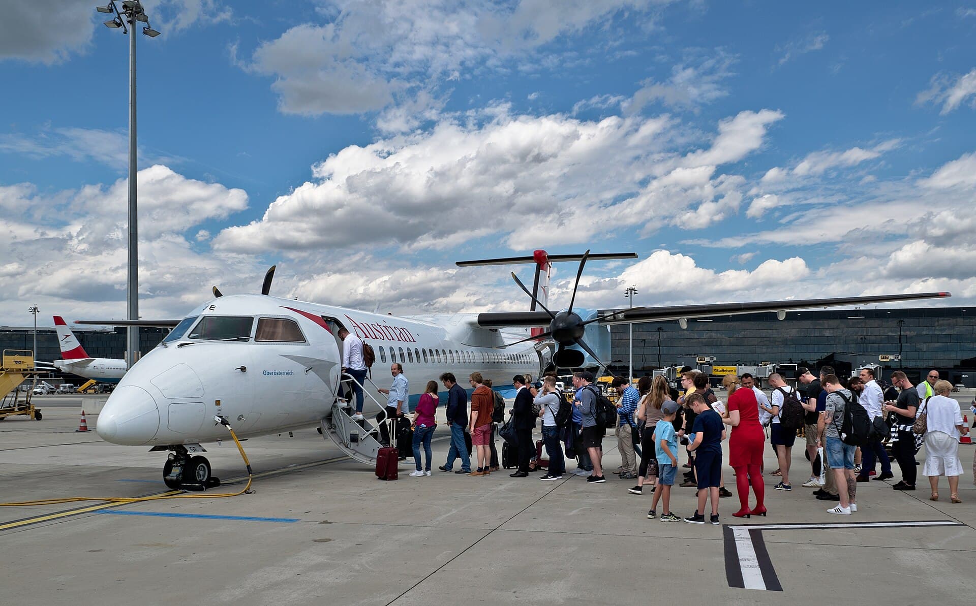 Passengers with cabin bags queuing to board a turboprop aircraft by stairs on the apron