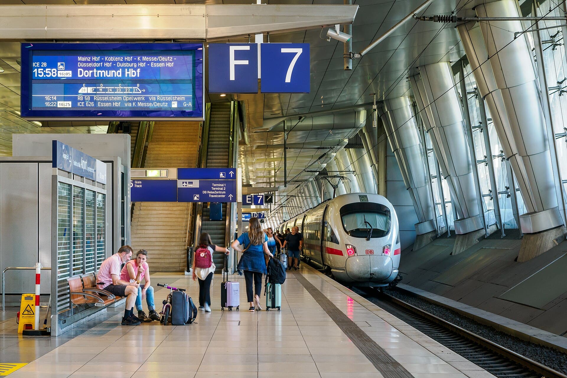 A high-speed train waiting at an airport railway station platform with travellers and their luggage