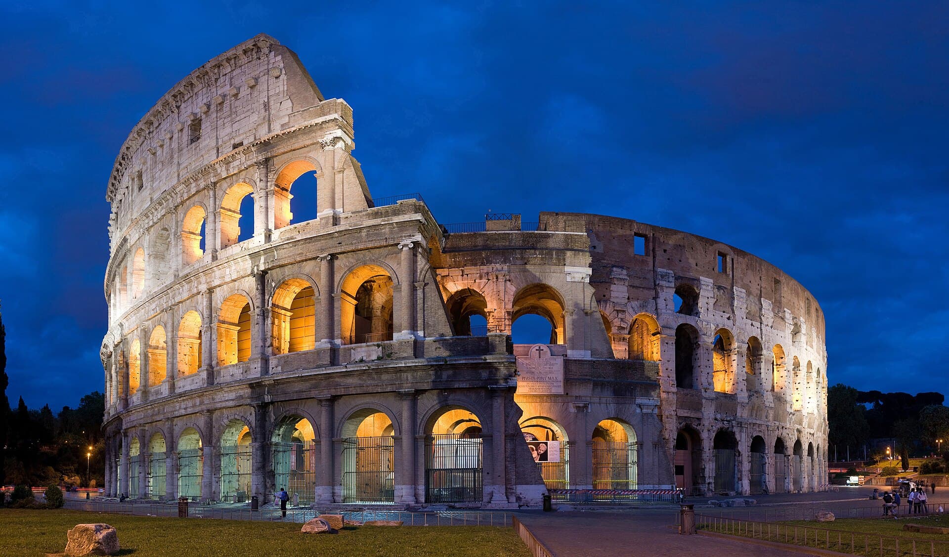 The Colosseum in Rome illuminated at dusk under a deep blue sky
